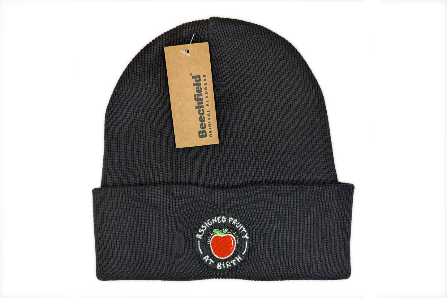 A photo of a black cuffed beanie with an LGBTQ+ pride design embroidered on the cuff. The design depicts a red apple with white text surrounding it reading "Assigned Fruity At Birth"