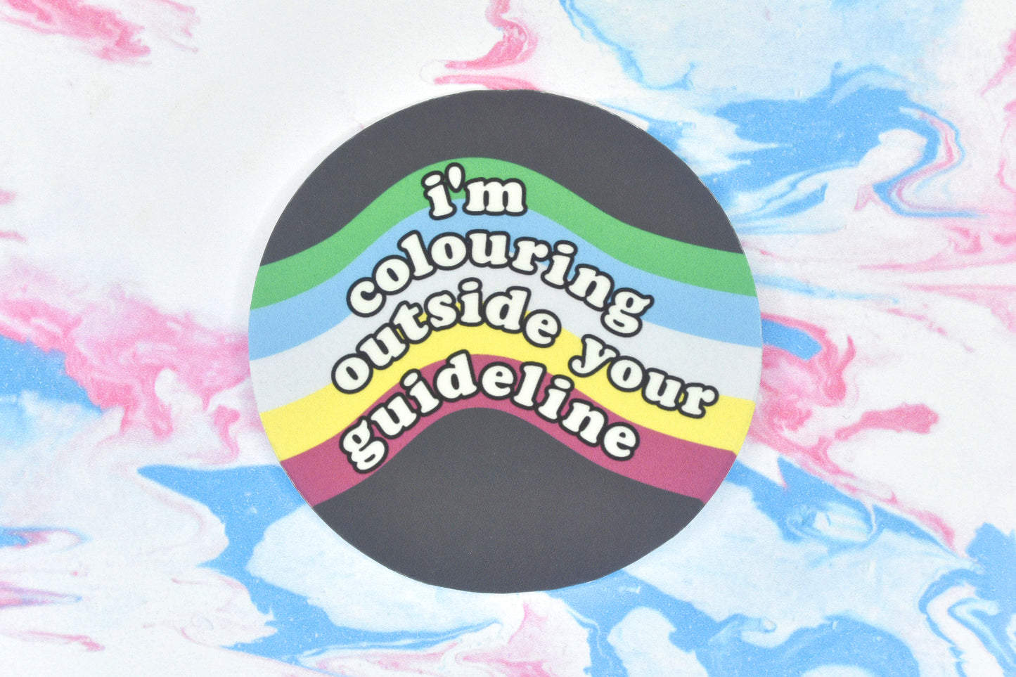 A circular vinyl sticker featuring the disability pride flag colours with text overlaid reading "I'm colouring outside your guideline".
