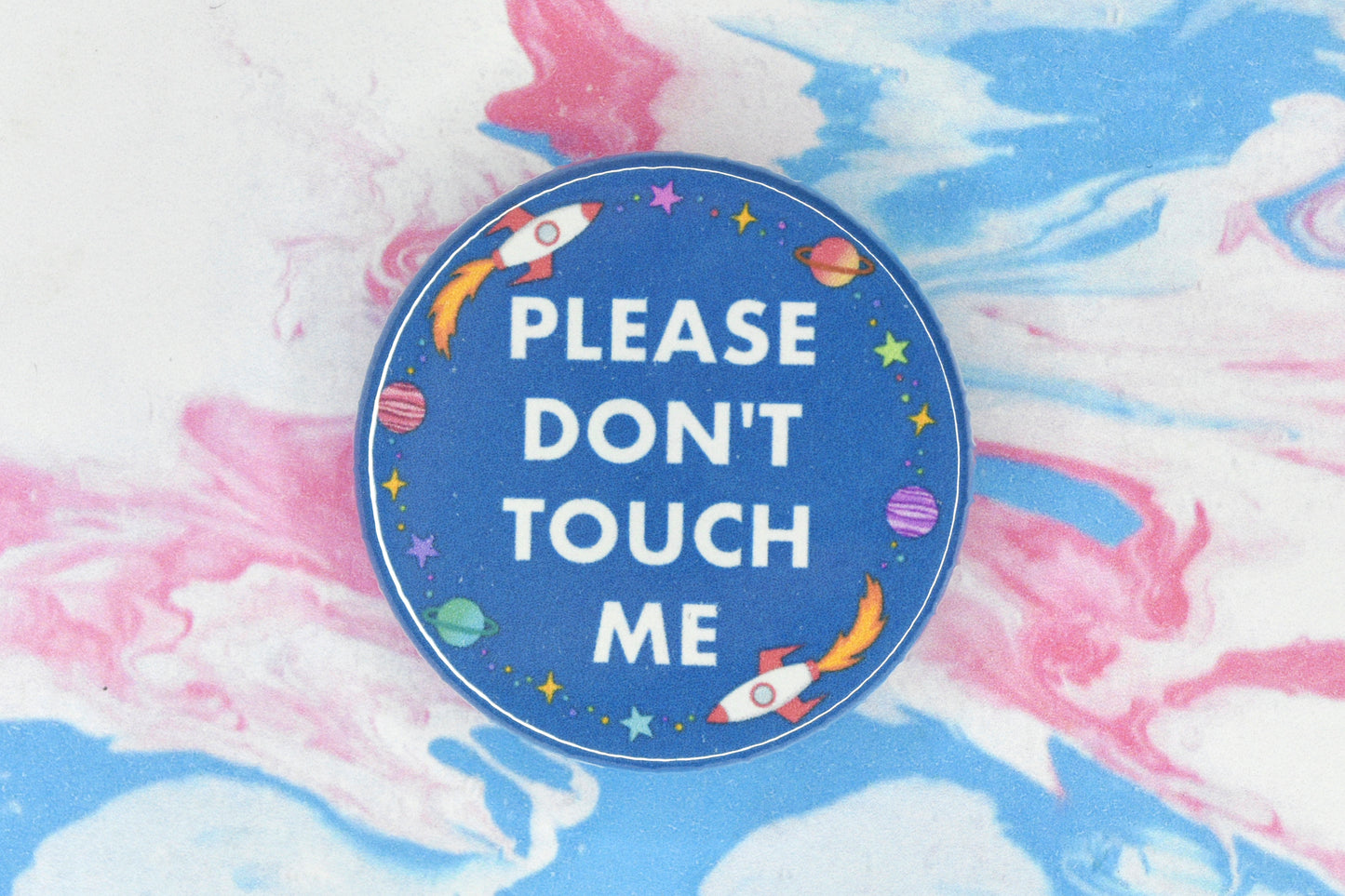 A hidden disability badge featuring a blue background and white text reading "Please don't touch me". There are space related illustrations surrounding the text including rockets, planets and stars.