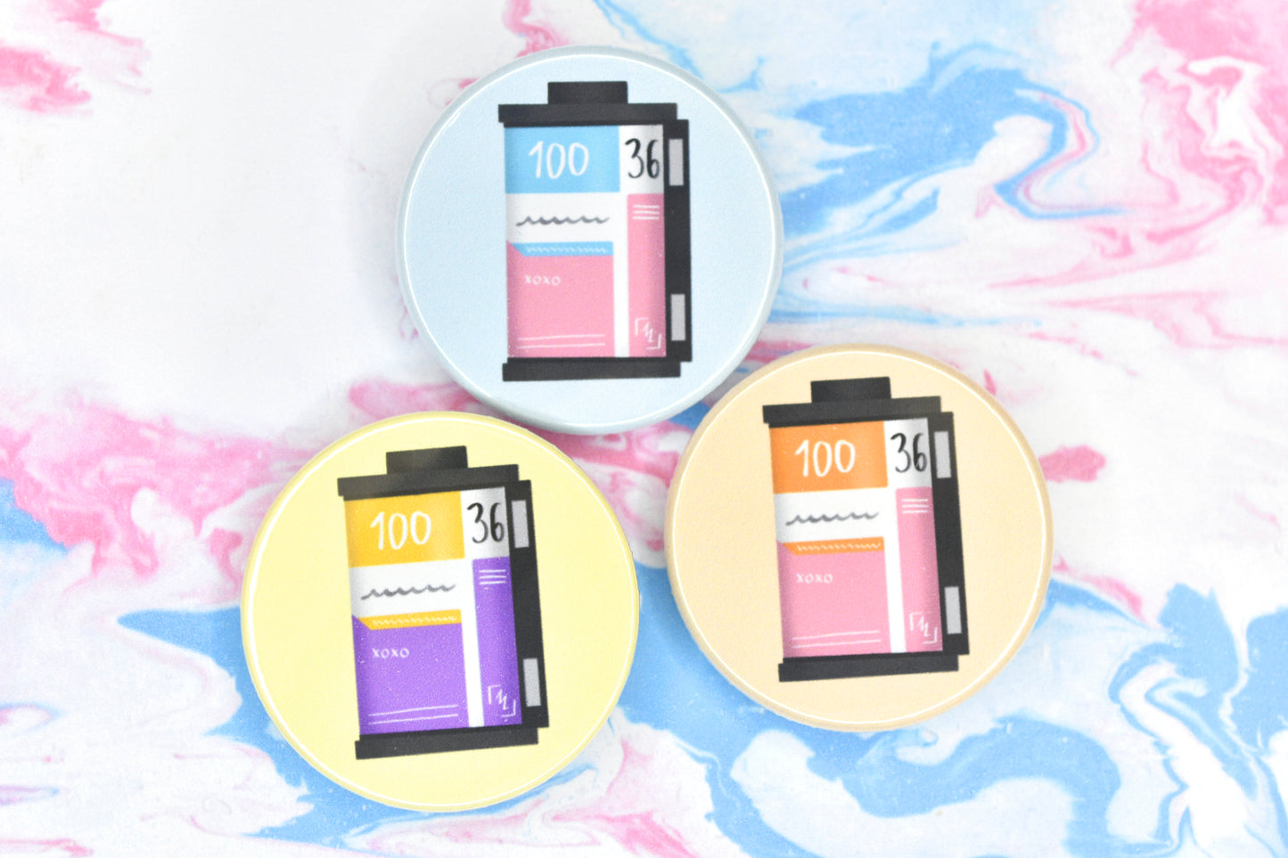 Three LGBTQ+ pride badges, each depicting a film roll in different pride flag colours. The flags are trans, non-binary and lesbian.
