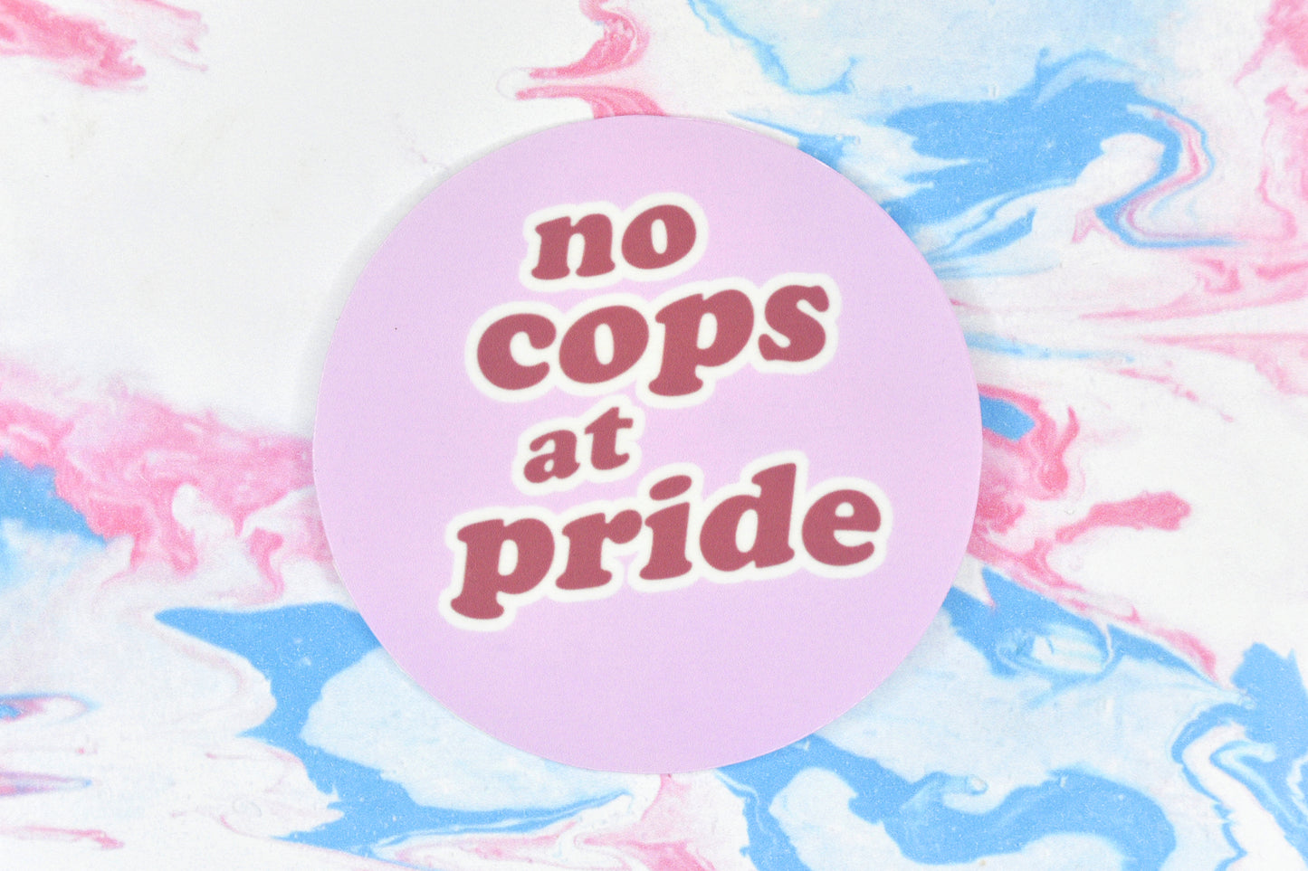 A circular LGBTQ+ vinyl sticker featuring dark pink text reading "no cops at pride" on a light pink background.