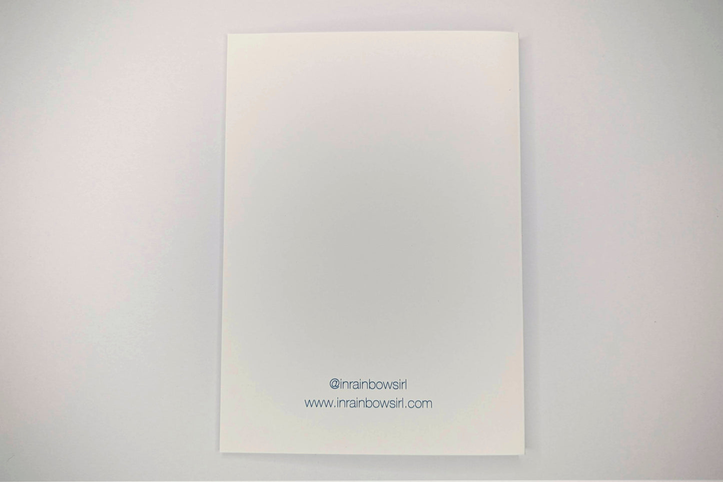 The back of the greeting card which is blank with the shop's social media handle and website printed at the bottom.