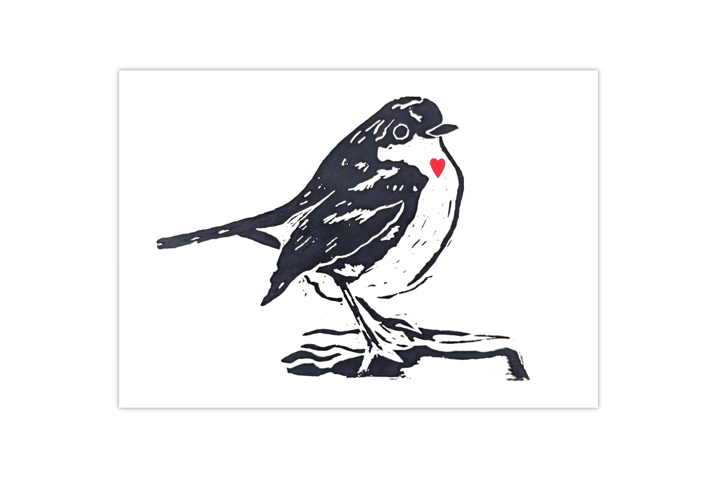 A tent fold greeting card featuring a lino print design of a robin printed in black ink on a white background with a small red heart over the bird's chest