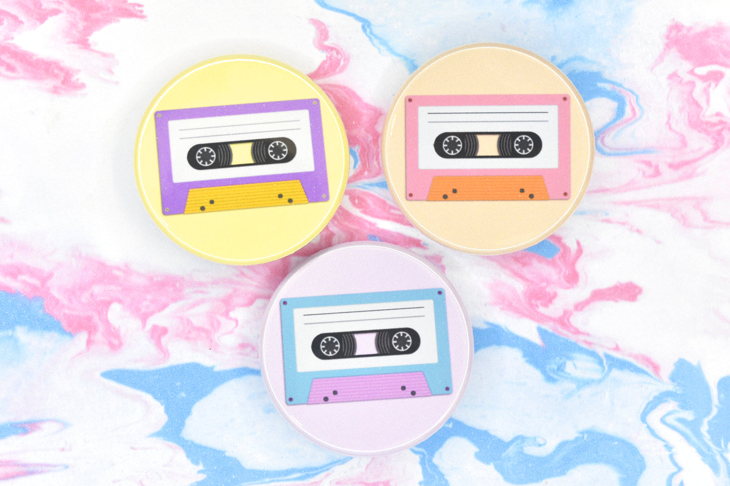Three LGBTQ+ pride badges, each depicting a cassette tape in different pride flag colours. The flags are non-binary, lesbian and trans.