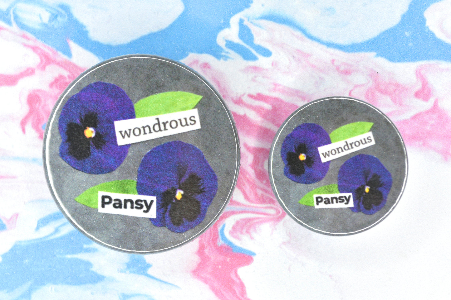 Button badges in two sizes featuring an LGBTQ+ pride collage design with text reading "Wondrous Pansy" and two small pansy flowers.