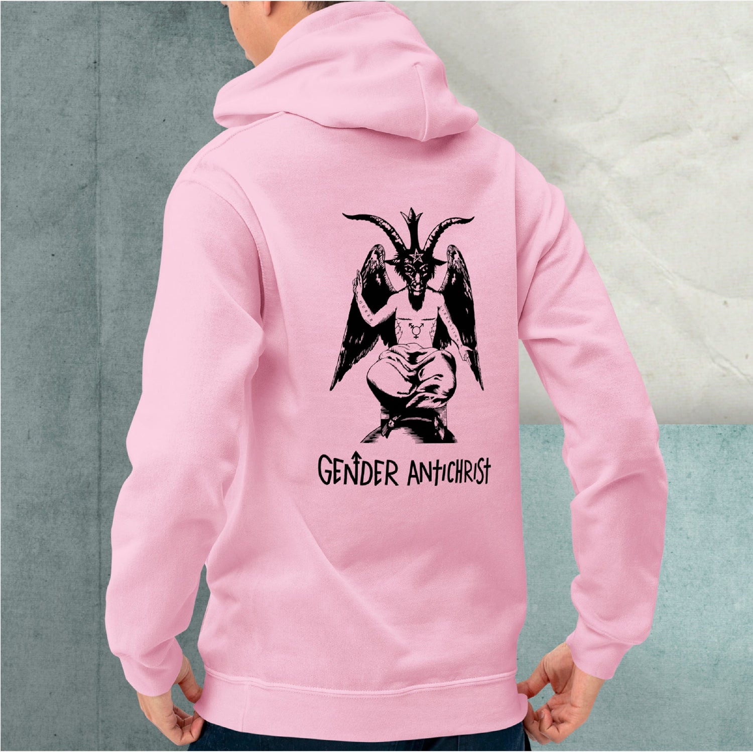 A model wearing a pink hoodie with an illustration on the back of Baphomet with top surgery scars, a trans symbol chest tattoo and the words queer and liberation tattooed on their right and left arms respectively. Below is text reading Gender Antichrist