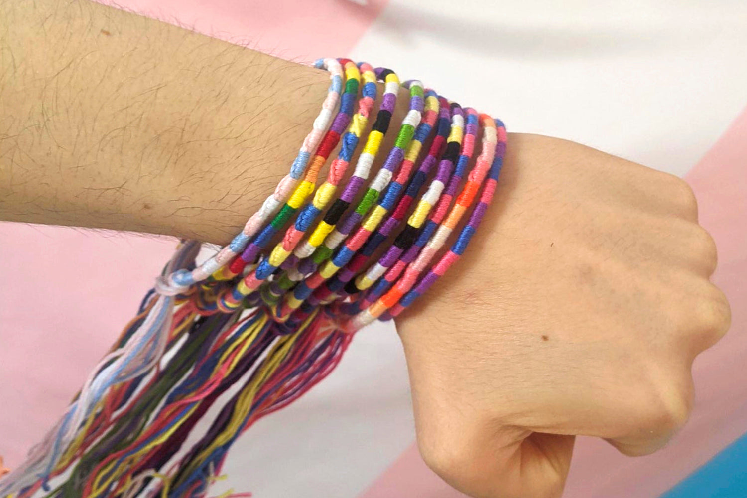 A collection of handmade pride bracelets made using embroidery thread in various pride flag colours. The flags shown include: rainbow, non-binary, bisexual, trans, lesbian and mlm. The bracelets are shown modelled on Alli's wrist.