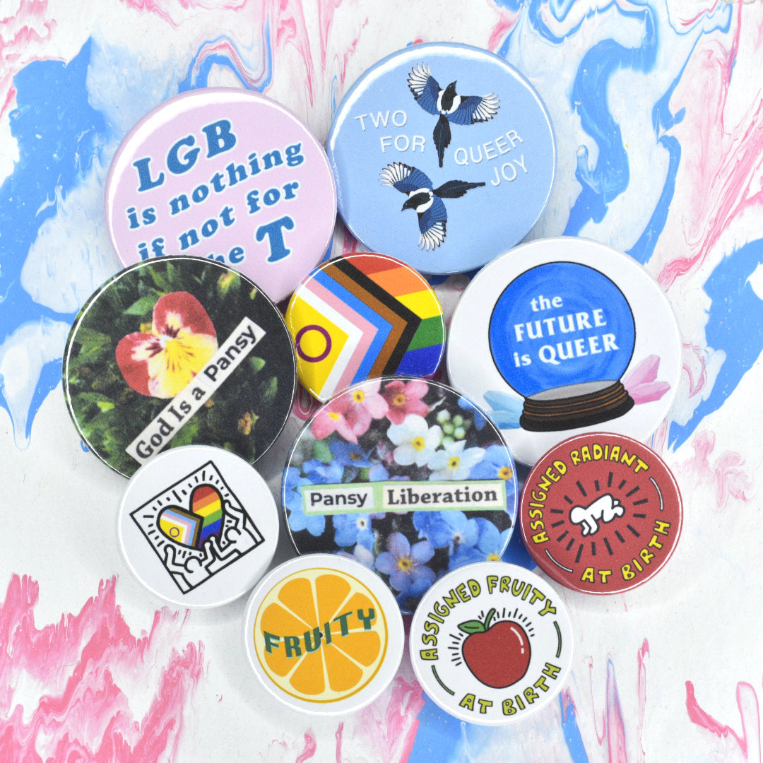 Ten In Rainbows badges, five small (Keith Haring progress pride heart, fruity orange, plain progress pride flag, assigned fruity, assigned radiant) and five medium (LGB for the T, two for queer joy, the future is queer, god is a pansy, pansy liberation)