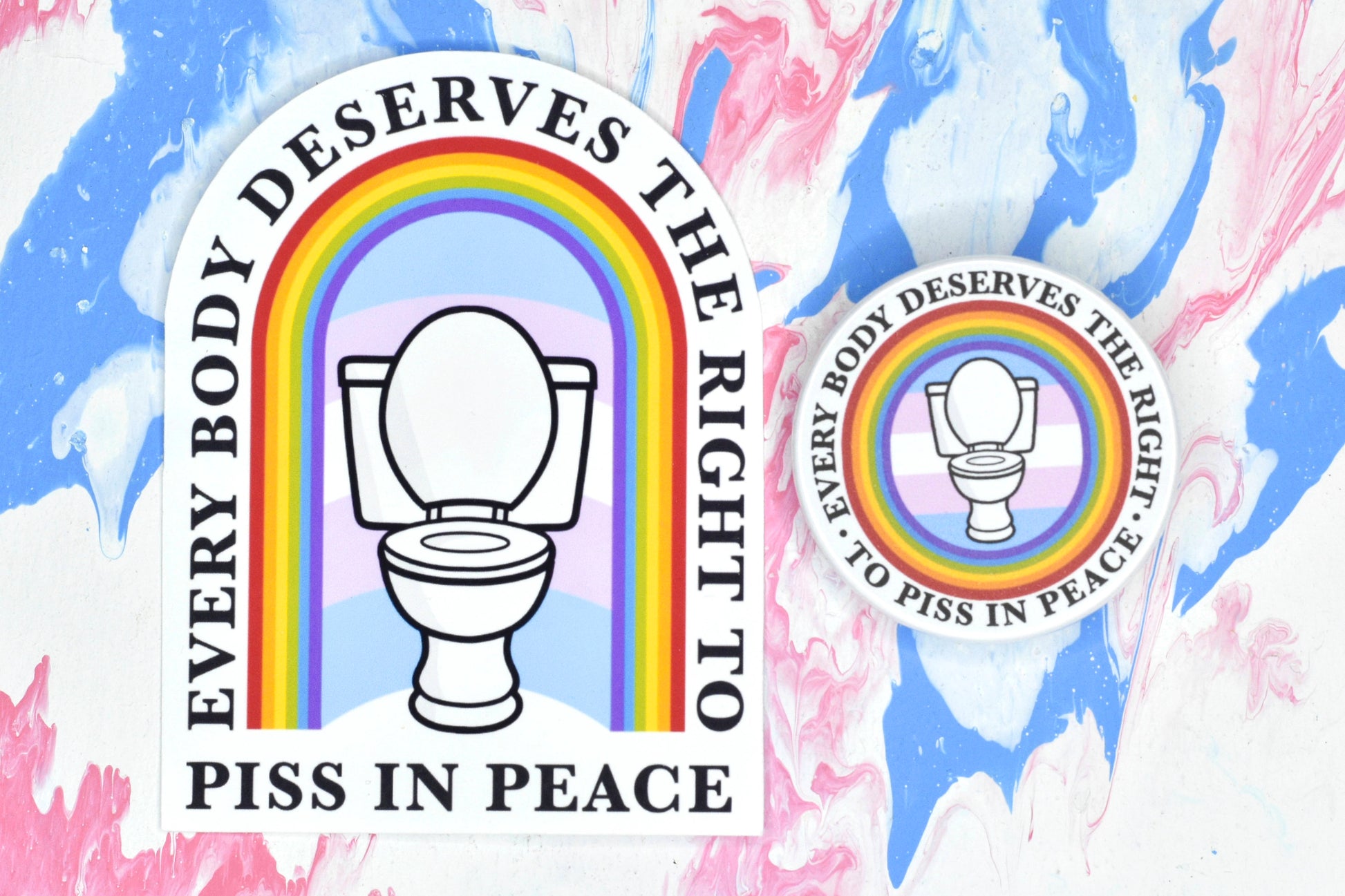 A tombstone-shaped sticker featuring a design depicting a white toilet in front of a trans pride flag with a rainbow archway over the top of it. There is text running along the outside and bottom of the archway reading "every body deserves the right to piss in peace". Next to this is a circular button badge featuring a circular version of the same design.