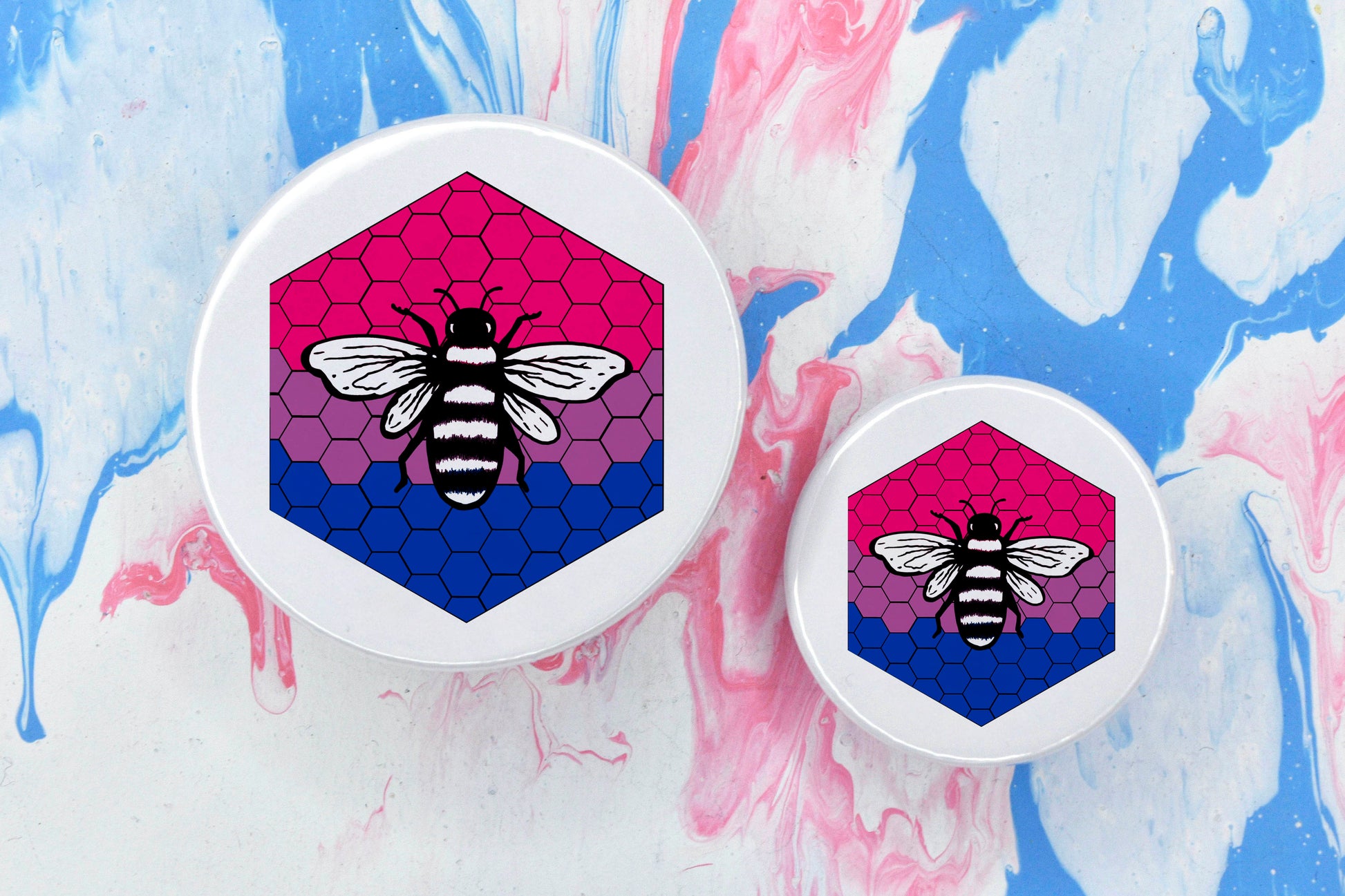 Two badges in sizes medium and small respectively, each featuring a white background with a black and white illustration of a bee overlaid on a bee hive pattern which is coloured in with the bisexual pride flag colours (pink, purple and blue).