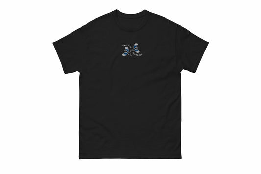 A mock-up of the front of a black t-shirt featuring an embroidered image of two magpies on the centre chest area with white embroidered text next around them reading "two for queer joy".