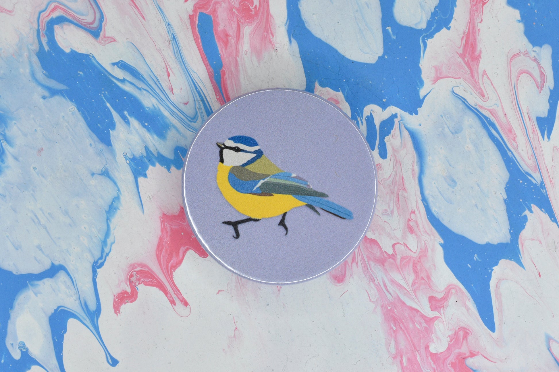 A circular pin badge with a pastel purple background featuring an illustration of a blue tit, a bird with blue, yellow, green and white markings.