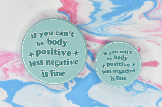 Two badges in sizes medium and small respectively, each featuring a light teal background with wavy bubble-like text in a darker teal shade reading "if you can't be body positive less negative is fine".