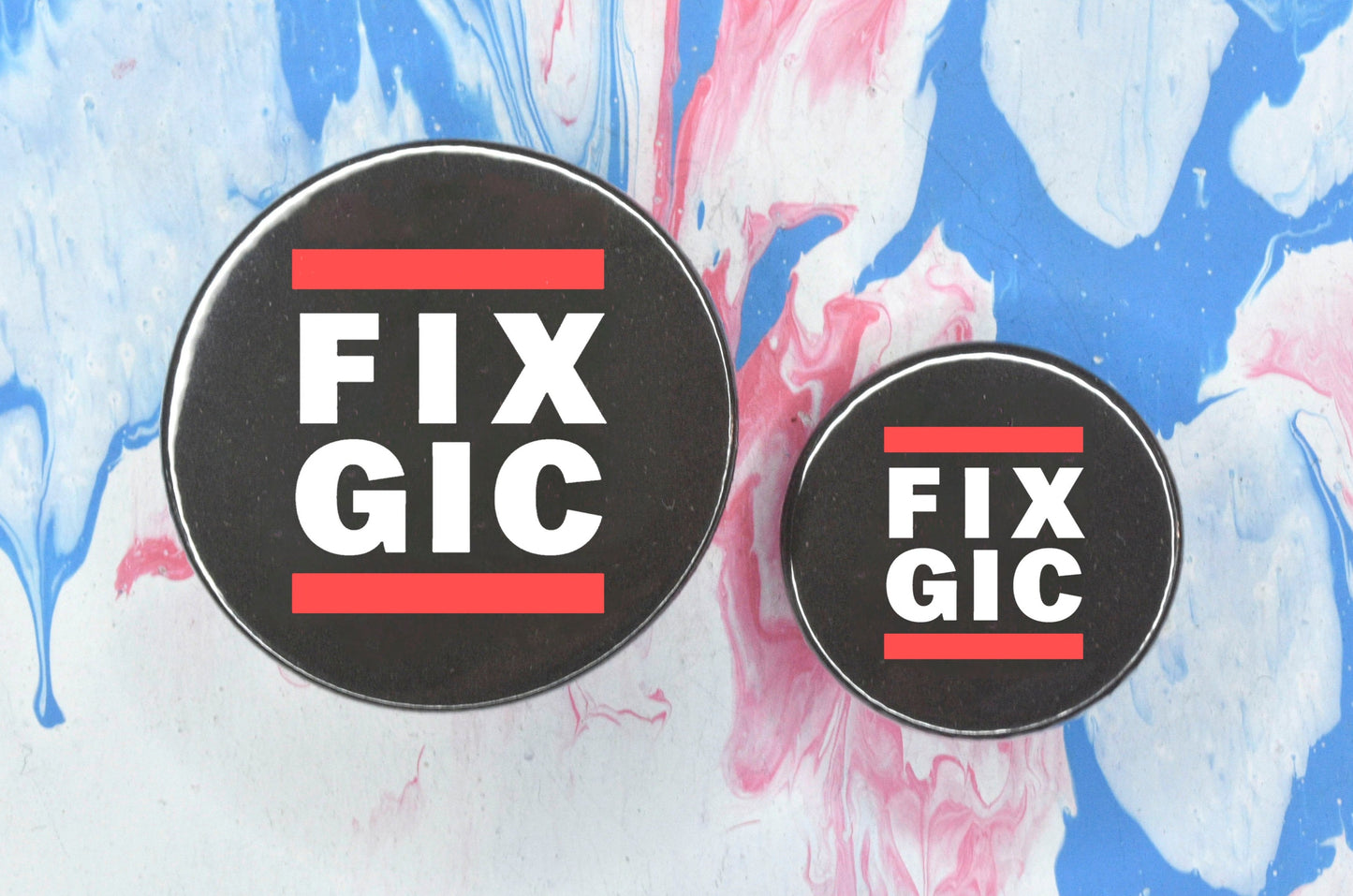 Two circular pin badges in sizes medium and small each with a black background, two rows of bold white upper case text and a solid red line above and below the text. The top row reads "fix" and the bottom row reads "gic".