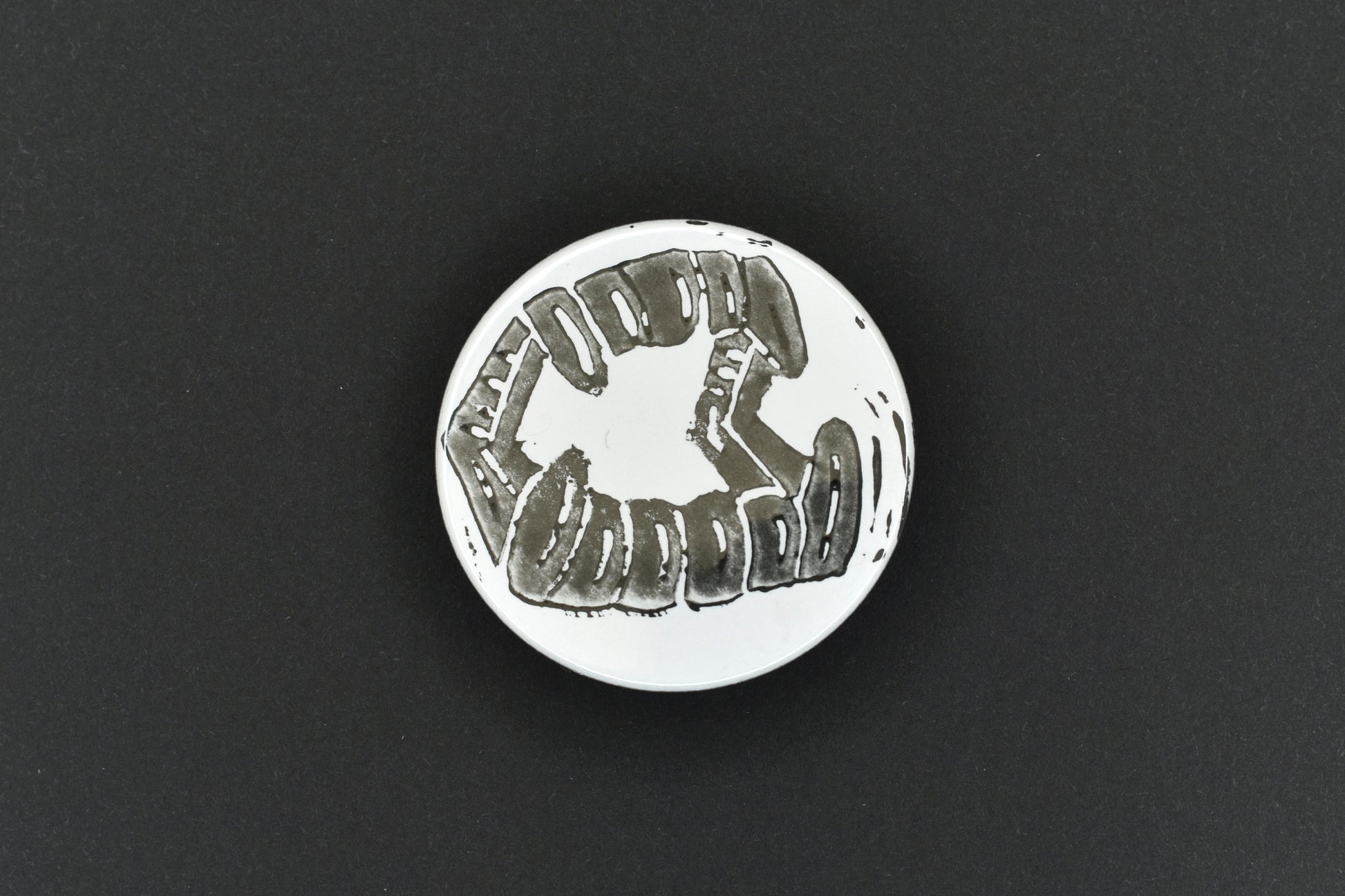 A single button badge featuring a white background with an original lino print stamped fang design in black ink.