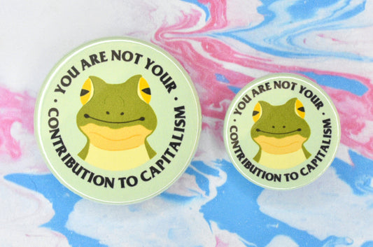 Two badges in sizes medium and small respectively, each featuring a green background with an illustration of a smiling frog in the centre. There is text surrounding the frog in a circle reading "you are not your contribution to capitalism".