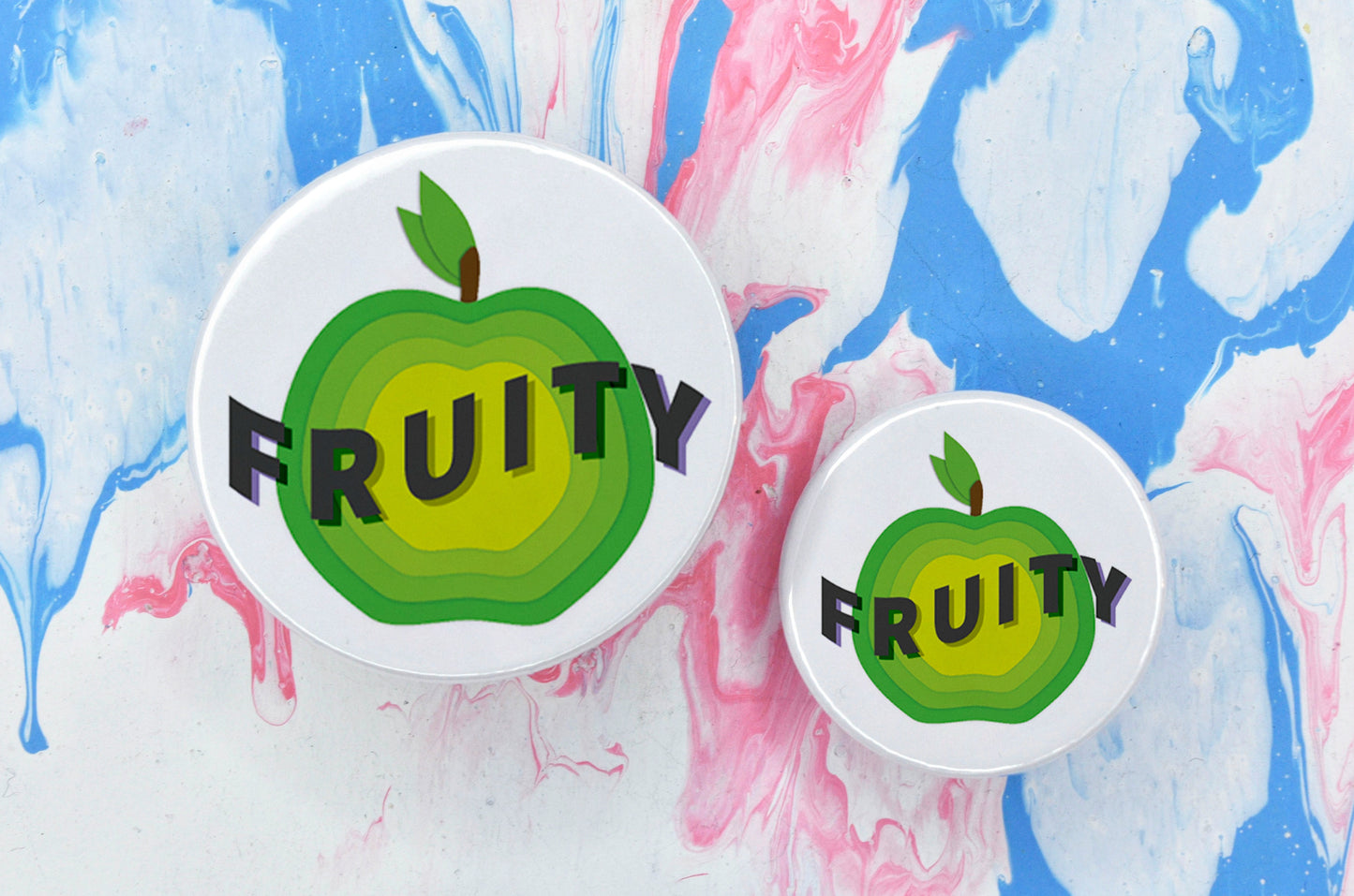 Two badges in sizes medium and small respectively, each featuring a white background with a green apple illustration. There is uppercase dark grey text across the centre of the apple reading "fruity".