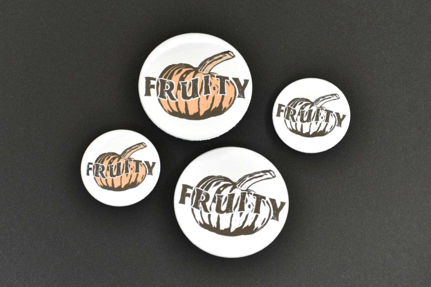 A collection of four badges, two of which feature an orange pumpkin with text reading "fruity" and two of which feature a black and white pumpkin with text reading "fruity".