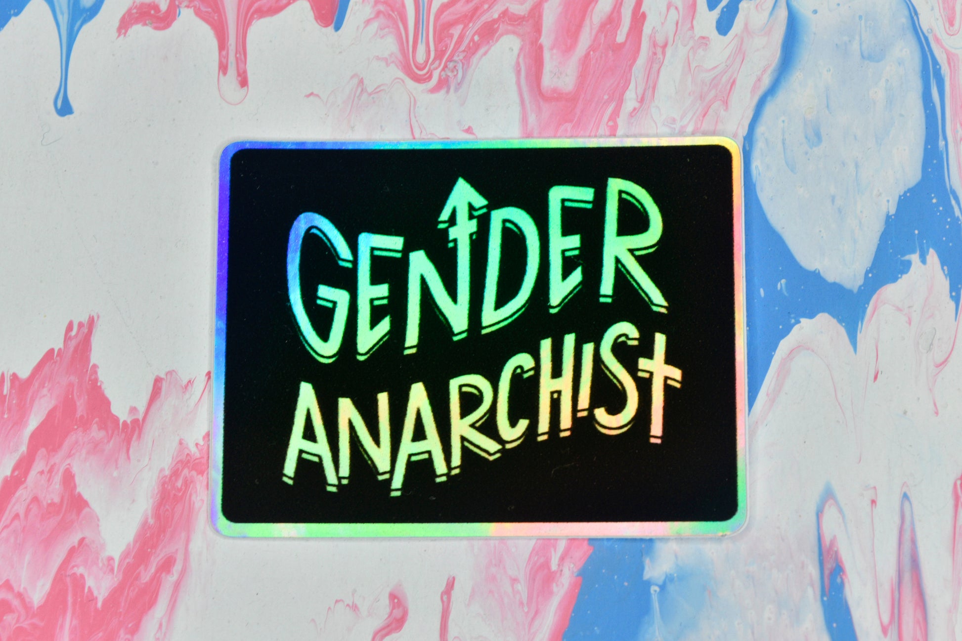 A rectangular holographic sticker with a black background and white holographic text reading "gender anarchist".