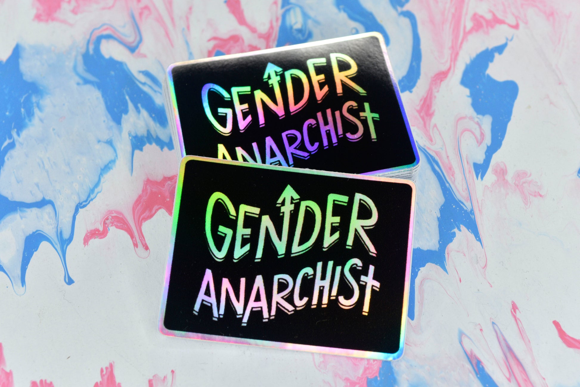 Two rectangular holographic stickers, both with a black background and white holographic text reading "gender anarchist".