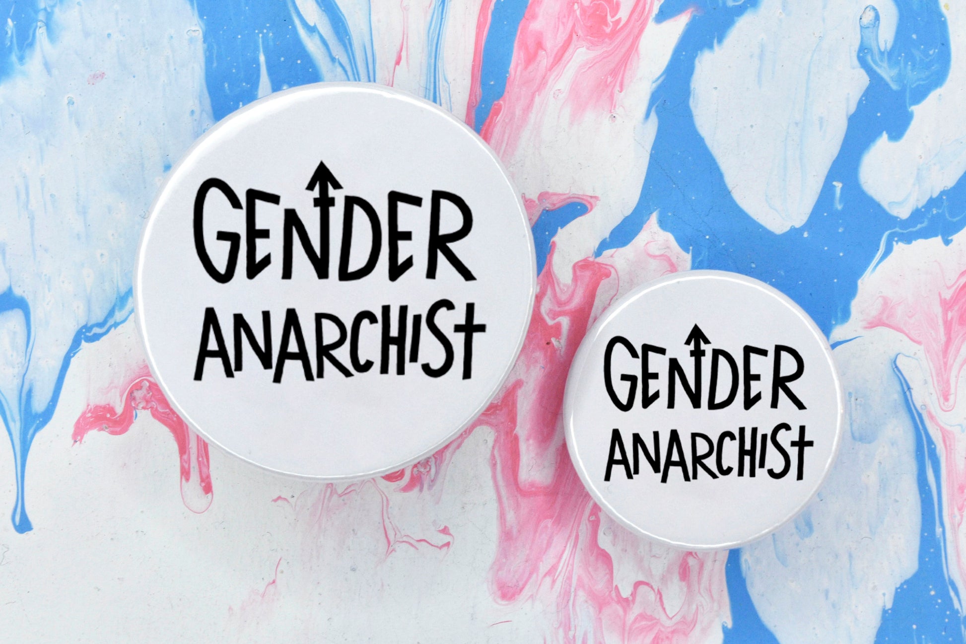 Two circular pin badges in sizes medium and small each with a white background and uppercase hand-drawn text in black which reads "gender anarchist".