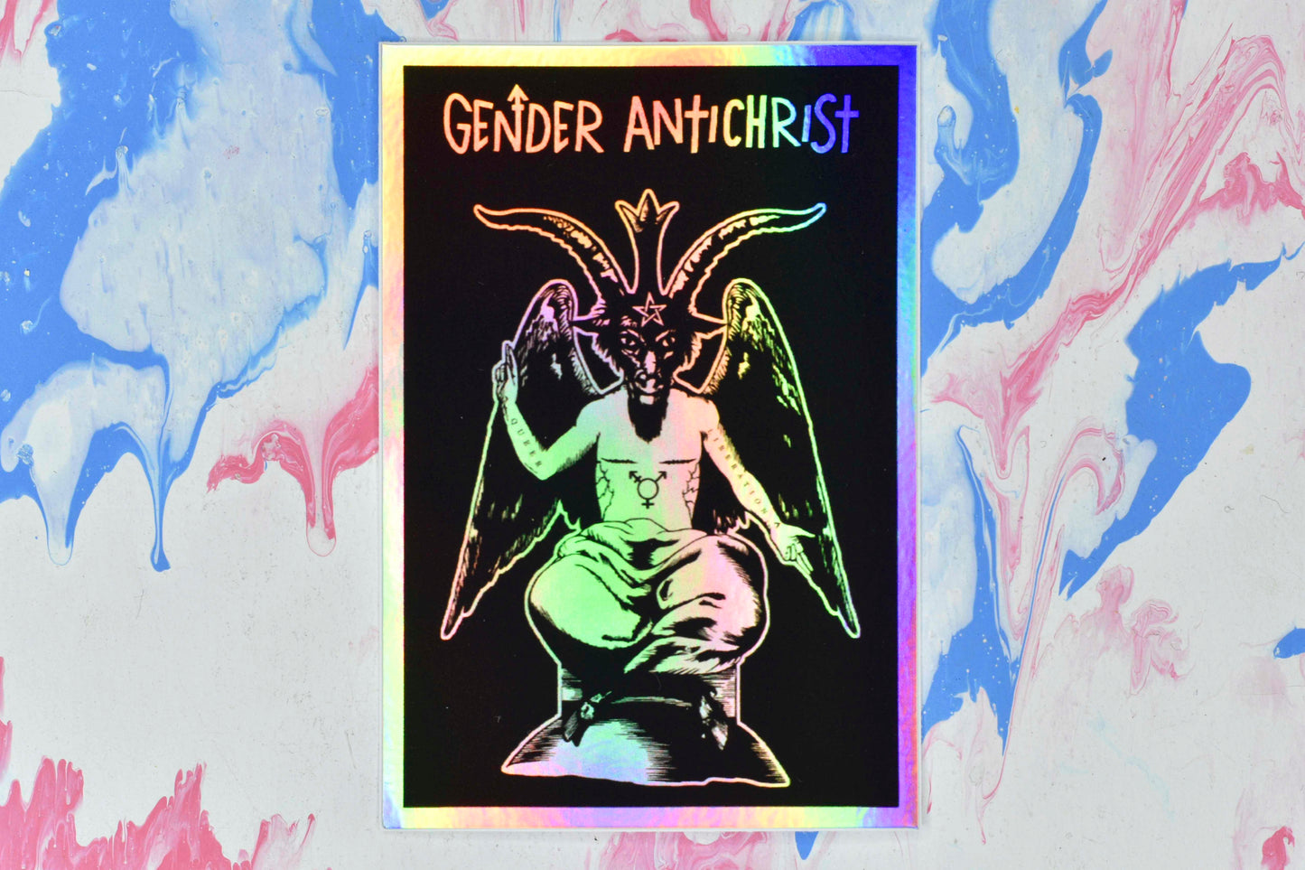 A rectangular holographic sticker with a black and white illustration of Baphomet, a figure with a human torso, a goat's head and hooves, and large angel-like wings. They have top surgery scars, a trans symbol tattoo on their torso and the words "queer" and "liberation" tattooed on their right and left arms respectively. Below Baphomet is white text reading "Gender Antichrist". The white areas of the design have a holographic effect over them which shifts and changes in the light.