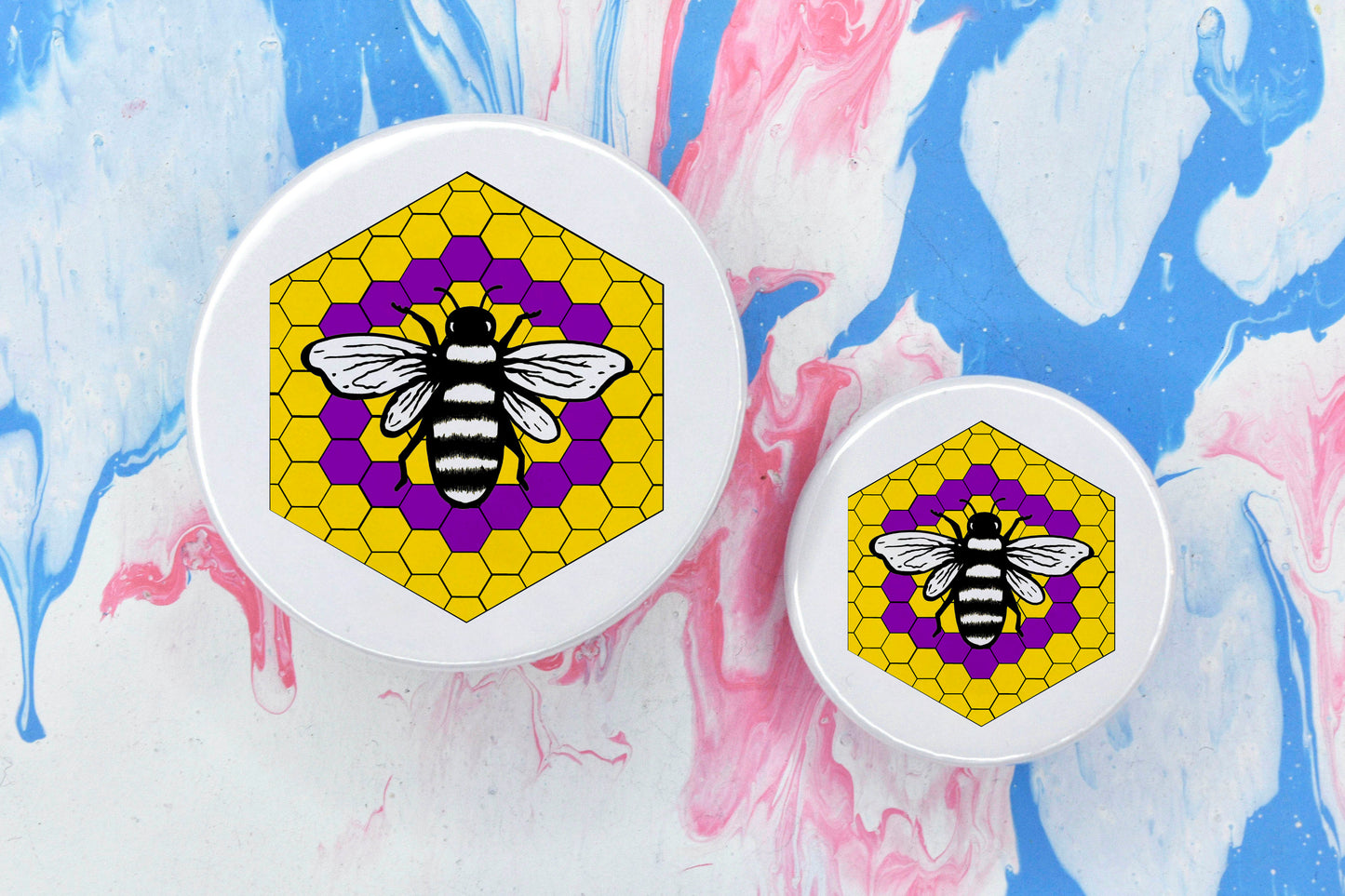 Two badges in sizes medium and small respectively, each featuring a white background with a black and white illustration of a bee overlaid on a bee hive pattern which is coloured in with the intersex pride flag colours (yellow with a purple circle in the centre).