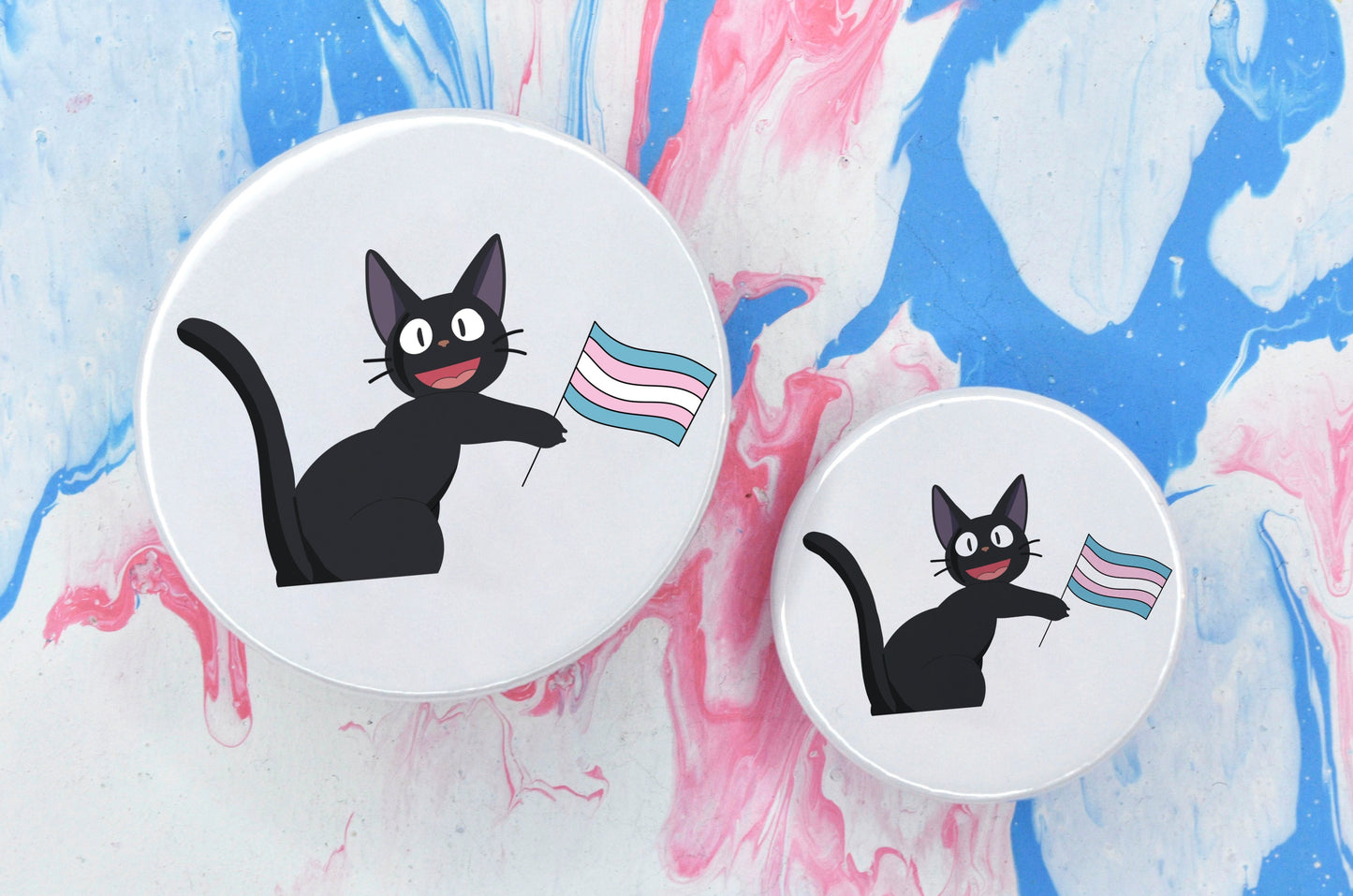 Two pin badges in sizes medium and small, both featuring an illustration of a black anime-style cat holding a trans pride flag. The background of the badge is white.