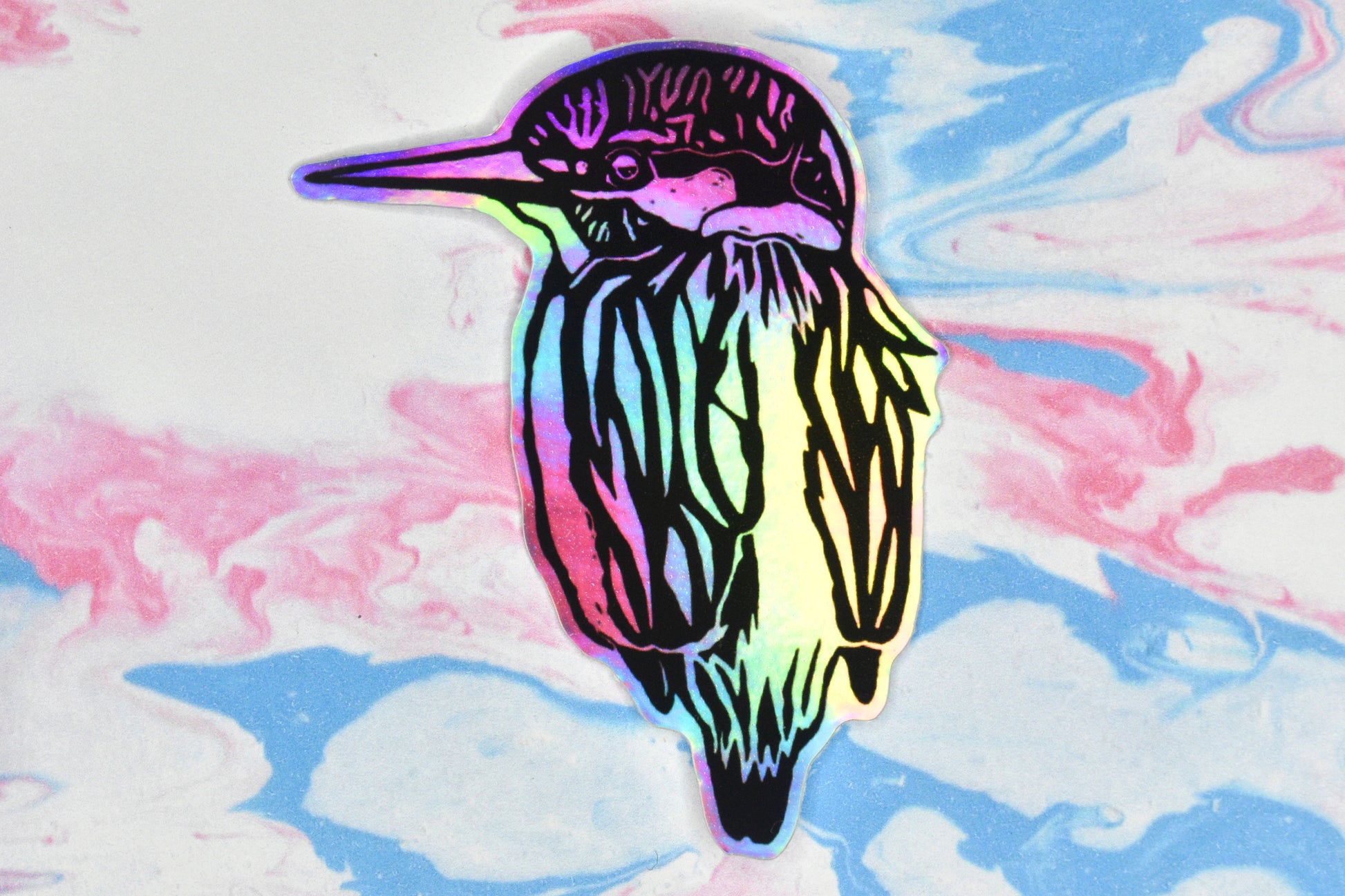 A sticker featuring a kingfisher illustration in black ink on an iridescent holographic background. The holographic effect produces a metallic rainbow of colour across the surface of the sticker.