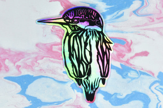 A sticker featuring a kingfisher illustration in black ink on an iridescent holographic background. The holographic effect produces a metallic rainbow of colour across the surface of the sticker.