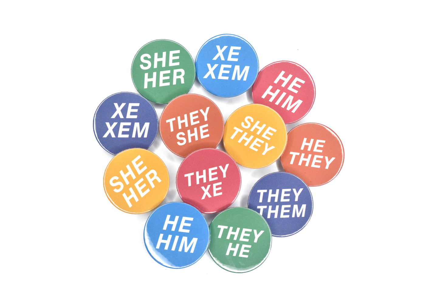 A selection of 12 pronoun pins, each with a solid colour background and white text featuring various sets of pronouns. The pins are shown in pink, orange, yellow, blue, green and purple. Pronouns shown include variations of he/him, she/her, they/them and xe/xem.