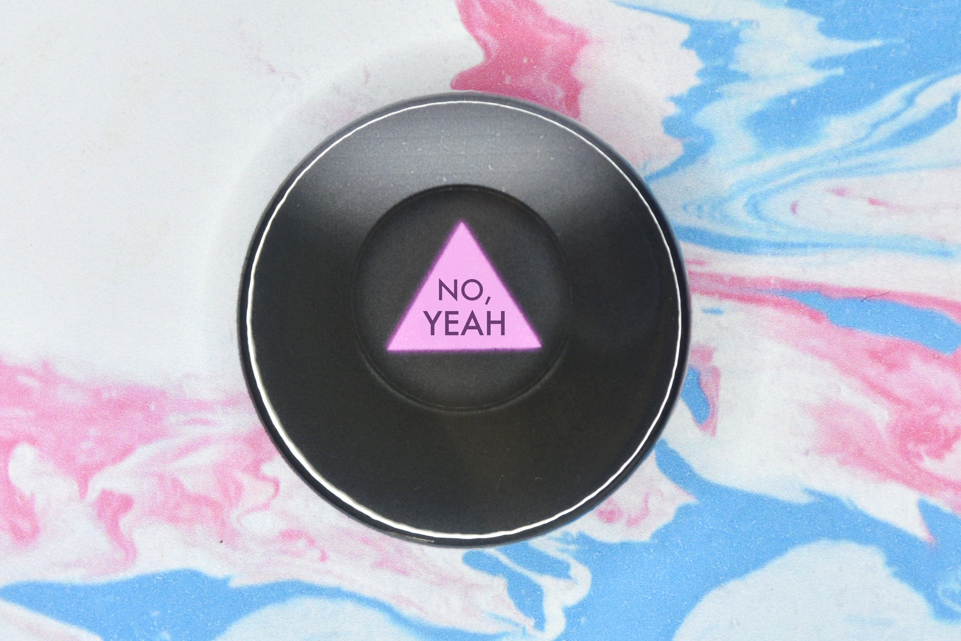 A circular badge in size medium featuring an illustration of a black magic 8 ball which takes up the full badge. There is a small circular window in the centre which shows a pink triangle with the message of the ball written on it in darker pink text. The text reads "No, Yeah".