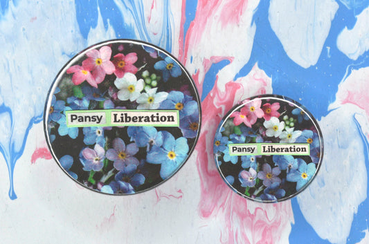 Two pin badges in sizes medium and small, both featuring a collage consisting of a photo of pink, white and blue forget-me-not flowers with newspaper print overlaid reading "pansy liberation".