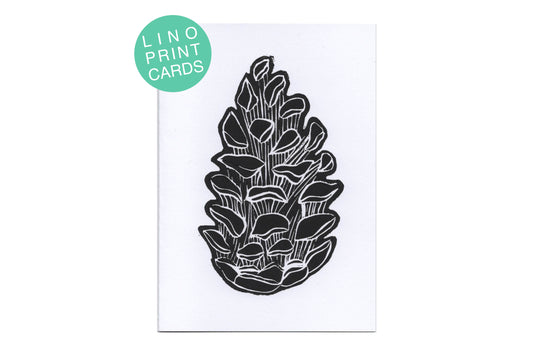 A lino print of a pine cone in black ink on white card. There is a teal circle label in the top left corner with white text reading "lino print cards"