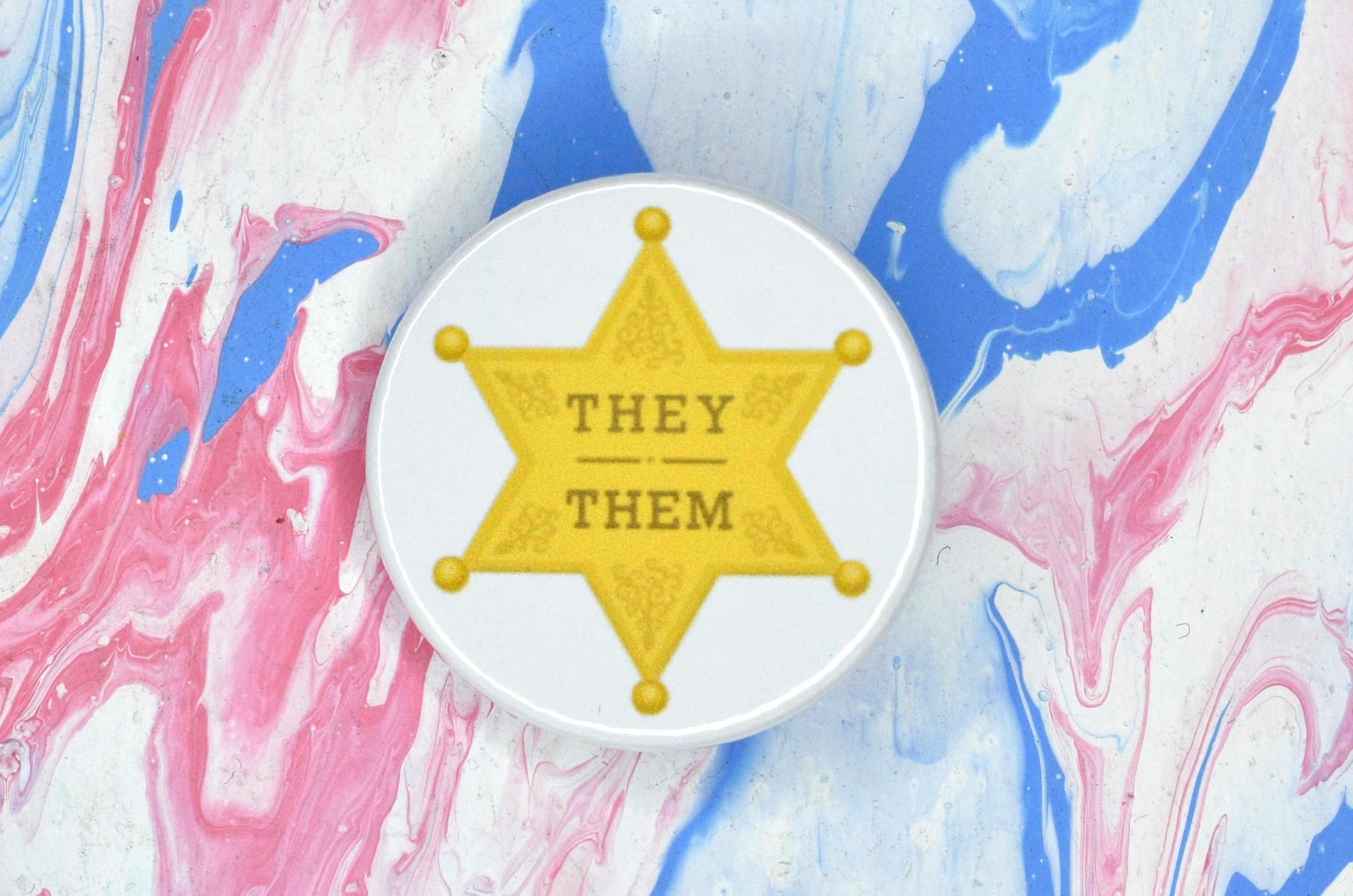 A badge featuring a white background with an illustration of a yellow/gold sheriff star. There is gold text on the star reading "they/them"