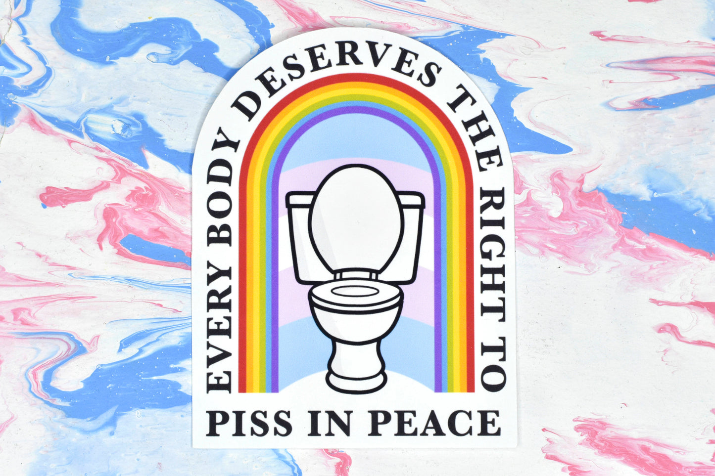 A tombstone-shaped sticker featuring a design depicting a white toilet in front of a trans pride flag with a rainbow archway over the top of it. There is text running along the outside and bottom of the archway reading "every body deserves the right to piss in peace".