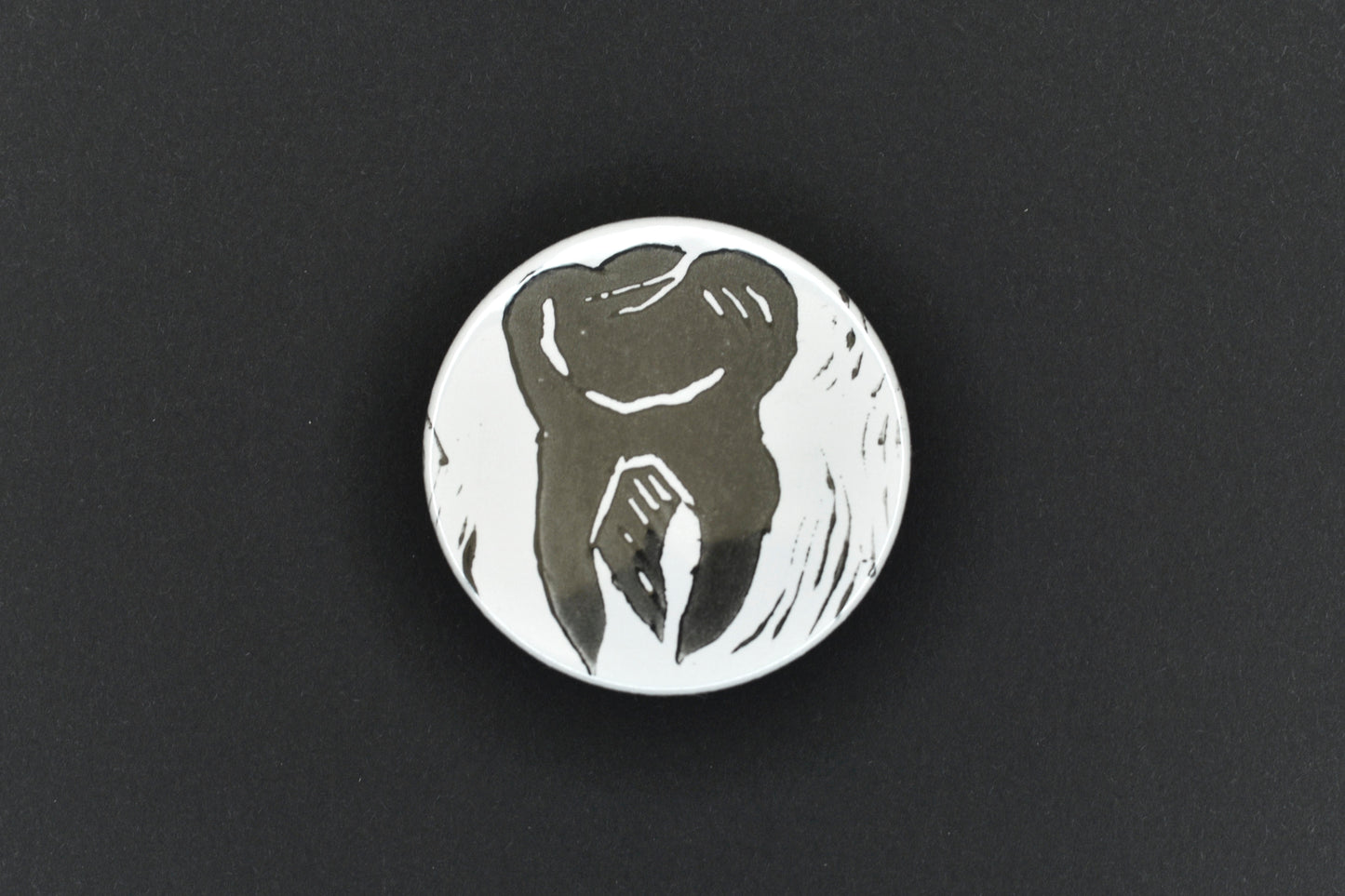 A single button badge featuring a white background with an original lino print stamped tooth design in black ink.