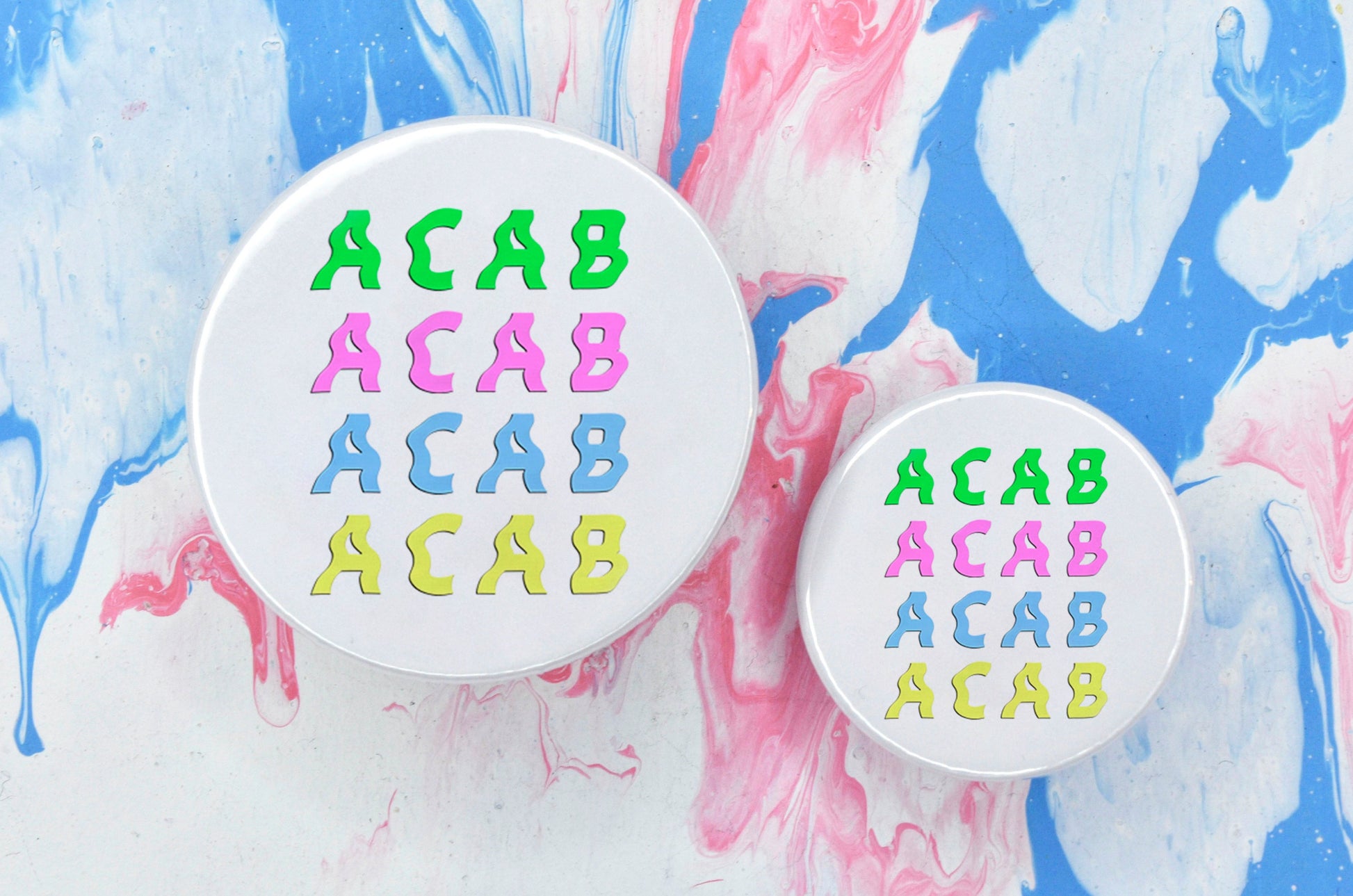 Two pin badges in sizes medium and small, both featuring four lines of wavy text reading "ACAB". Each line of text is a different pastel colour: green, pink, blue and yellow. The badge background is white.